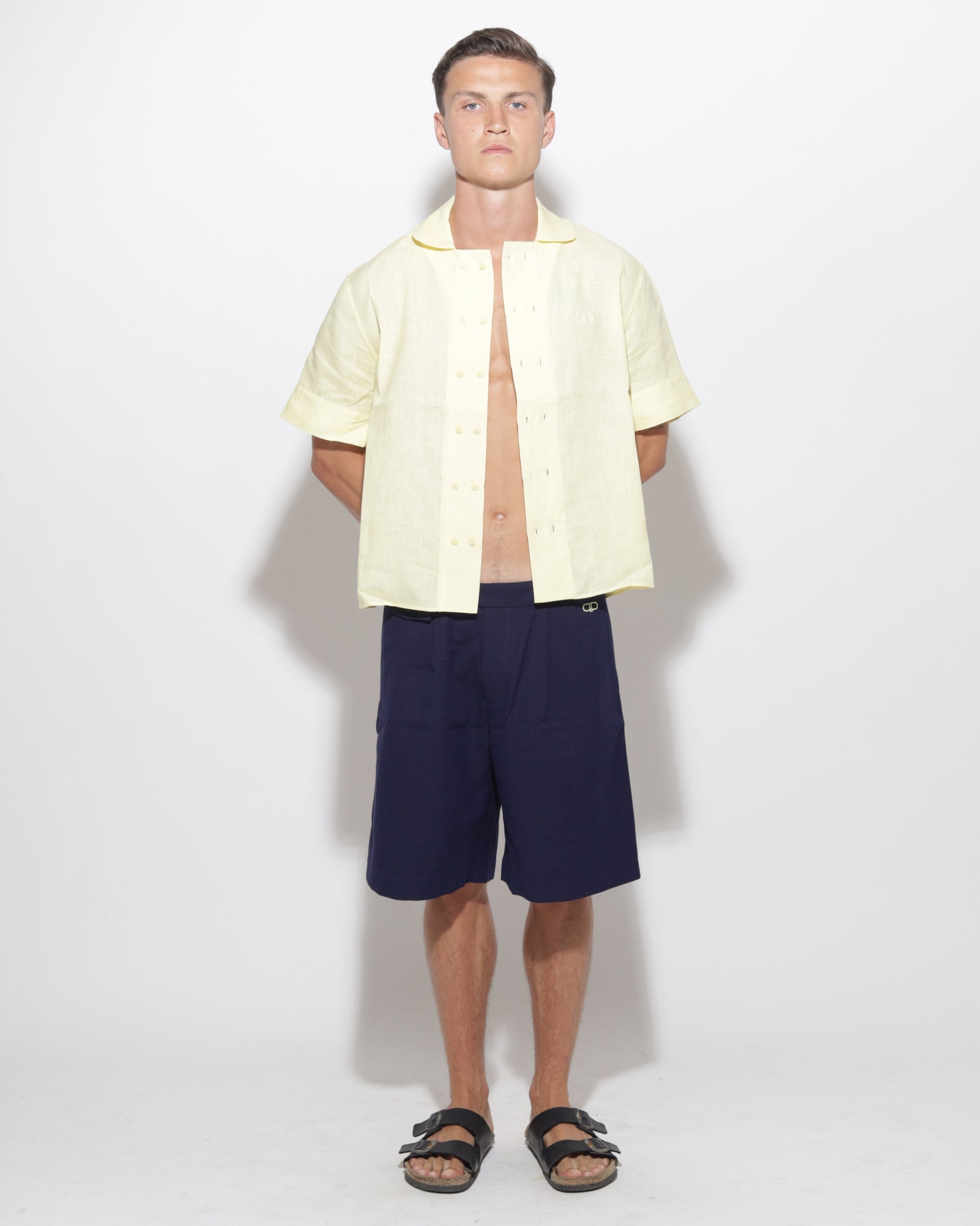 Man wearing a light yellow shirt and navy shorts on a white background