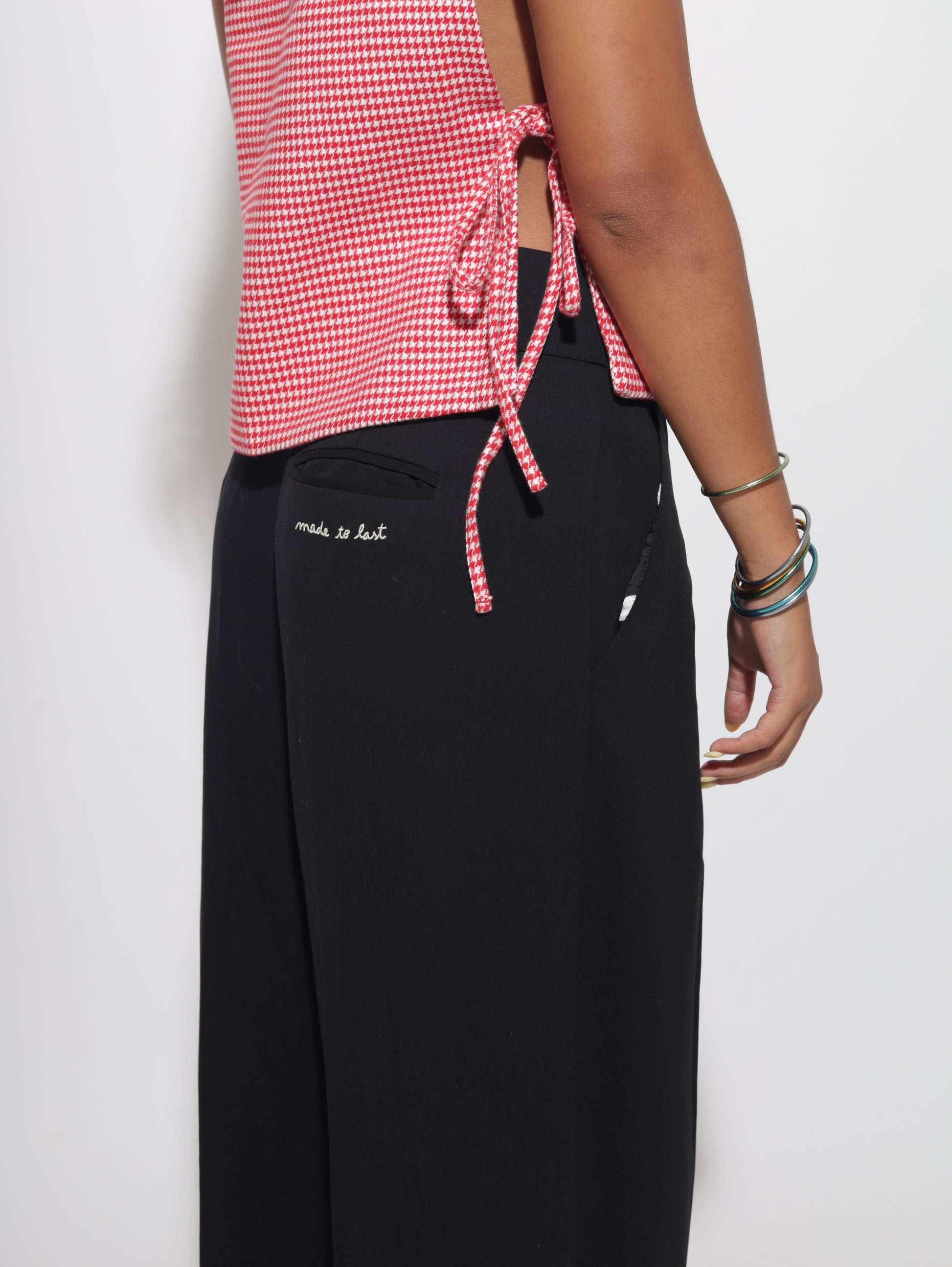 Person wearing black pants with a red and white checkered vest on a white background