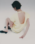 Woman wearing a yellow dress with an open back sitting on a white floor.